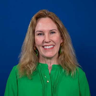 A white woman with long, dark blond hair wearing a green shirt, smiling at the camera.