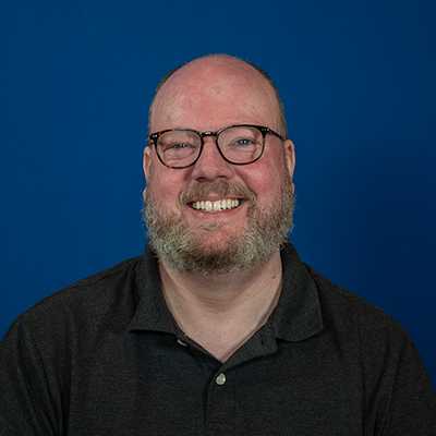 A white male with no hair and glasses, wearing a grey polo shirt.