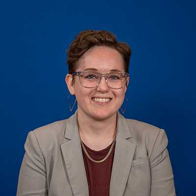 A white person in their 30s with short, light brown hair wearing glasses and a grey blazer.