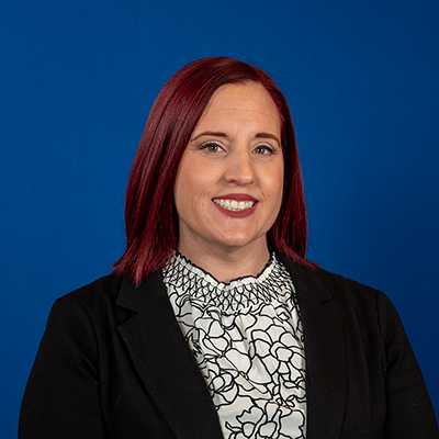 A white woman with medium length, colored-red hair smiling at the camera.