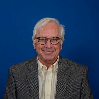A white male with white hair and eyeglasses, smiling.